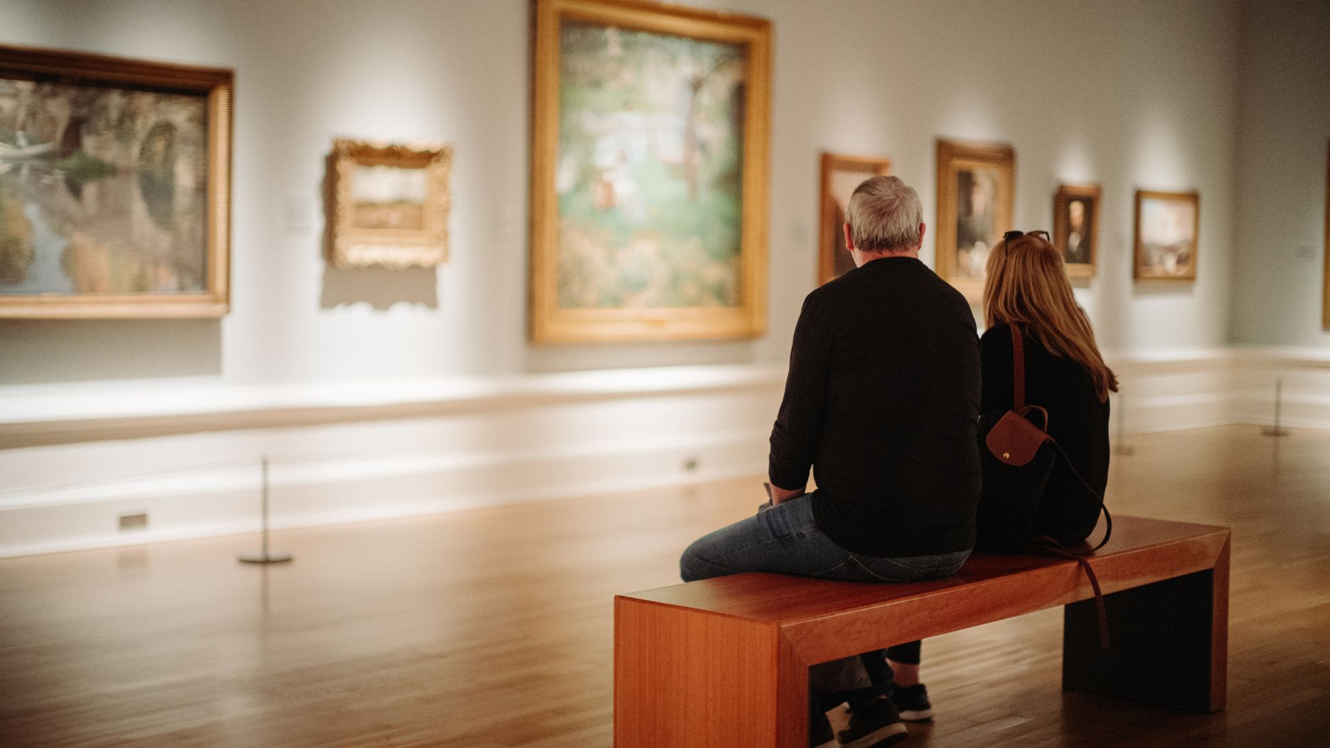 A man and a woman sit on a bench observing paintings at Ulster Museum.