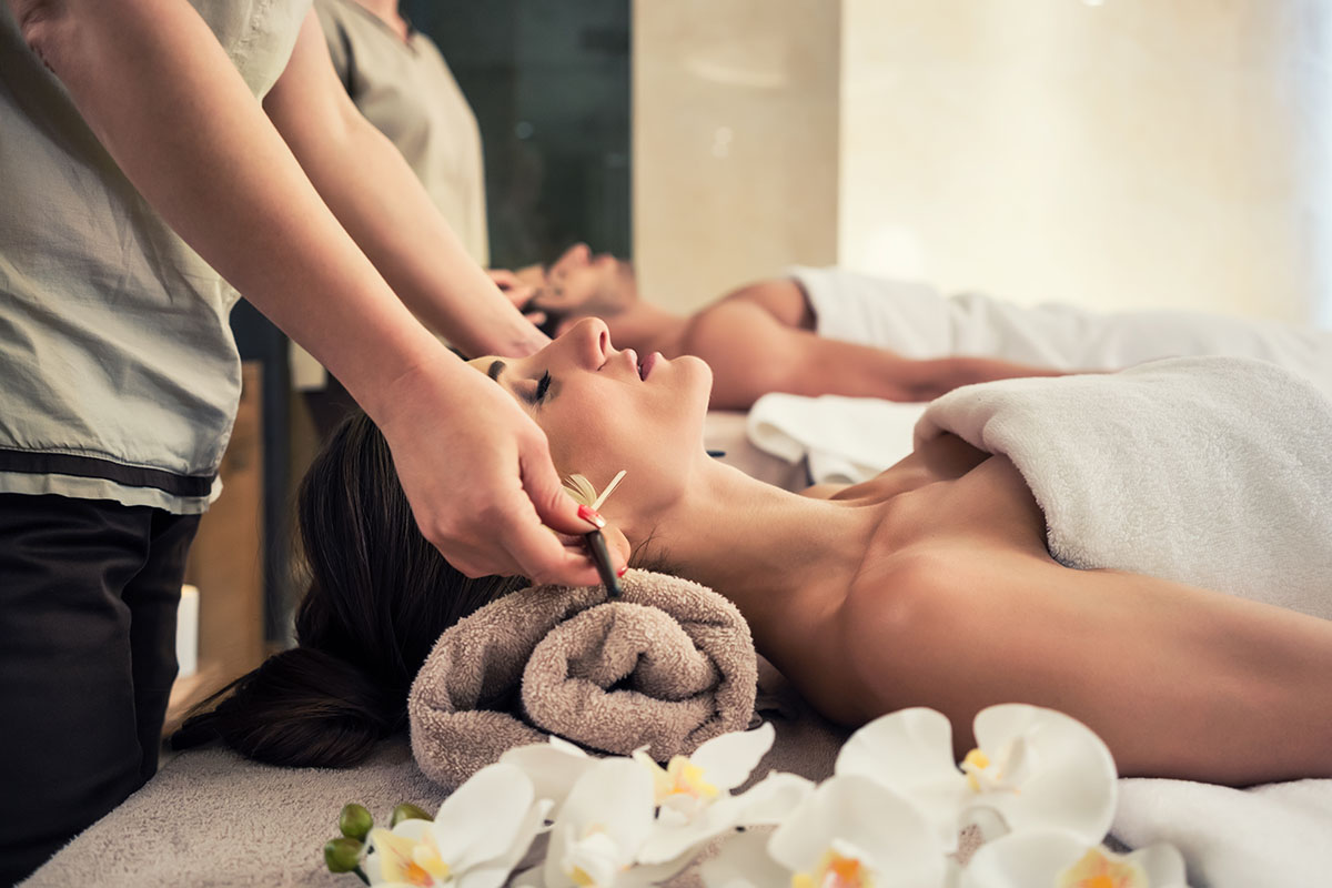 Two people lying on spa beds and a masseuse standing